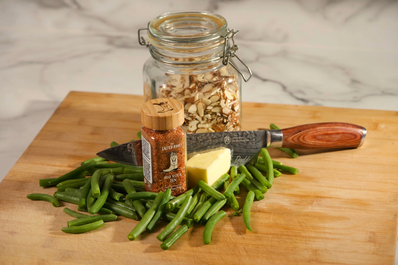 Fresh green beans, butter, sliced almonds and a jar of The Salted Roots Red Rock Zen on a cutting board