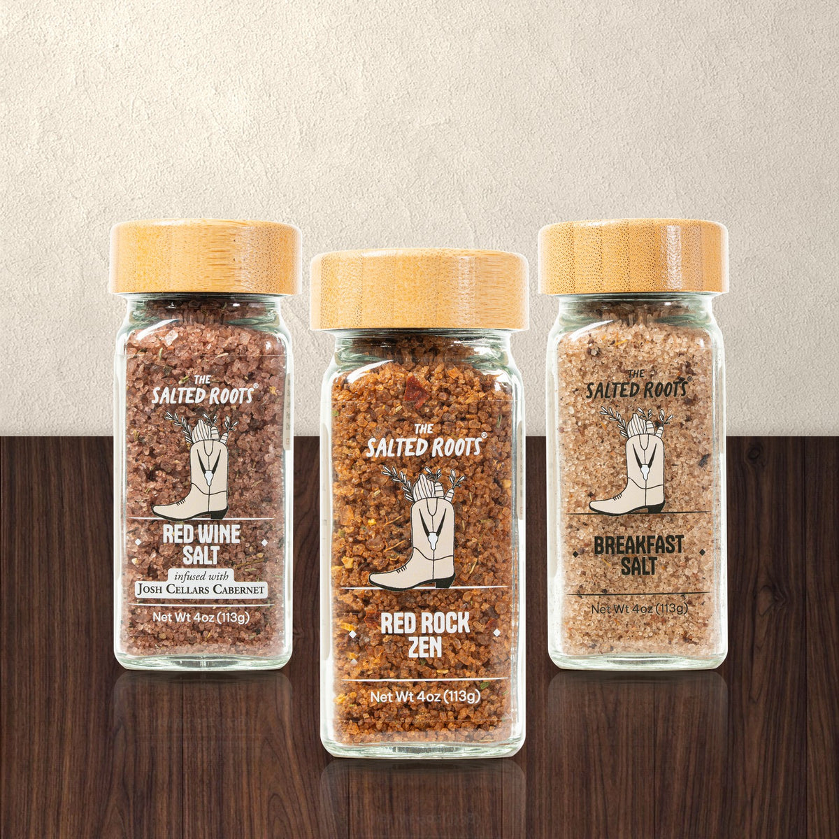 Three jars of The Salted Roots infused salt on a walnut table: Red Wine Salt, Red Rock Zen and Breakfast Salt